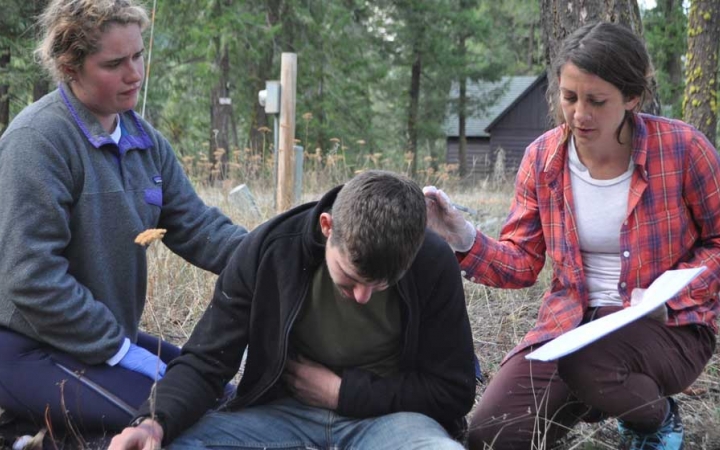 three people participate in a wilderness first responder exercise